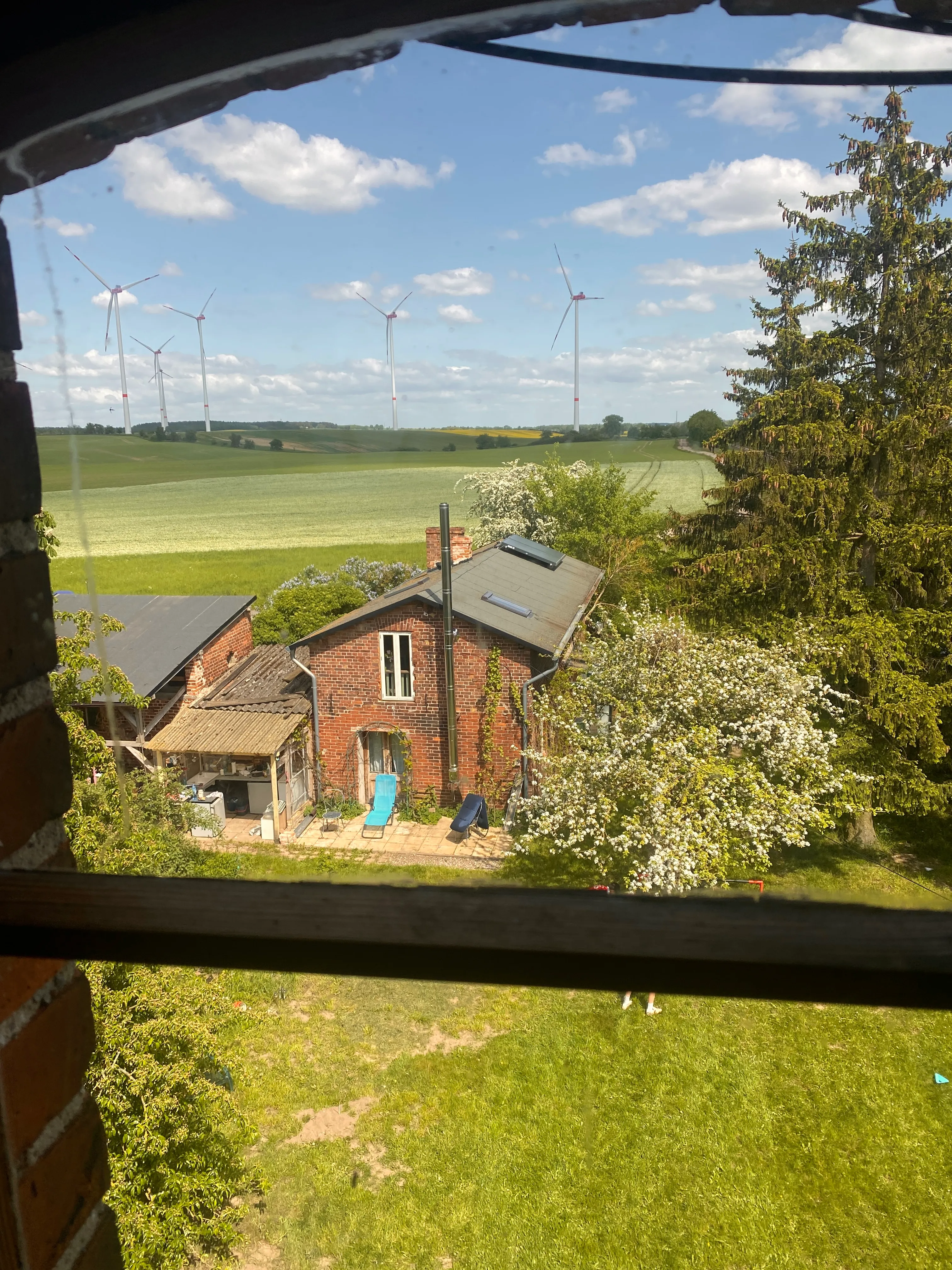 Ein 2-stöckiges rotes Backsteinhaus mit Garten und Windrädern am Horizont.